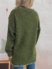 Person wearing a green knitted sweater with a white brick wall background