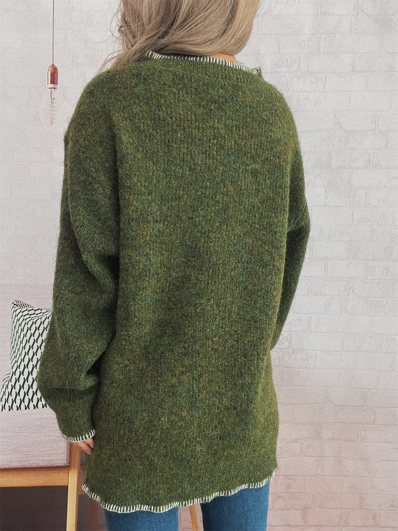 Person wearing a green knitted sweater with a white brick wall background