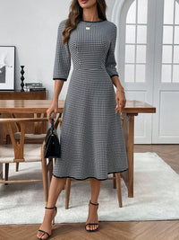 Woman in a black and white checkered dress standing in a room with wooden furniture.