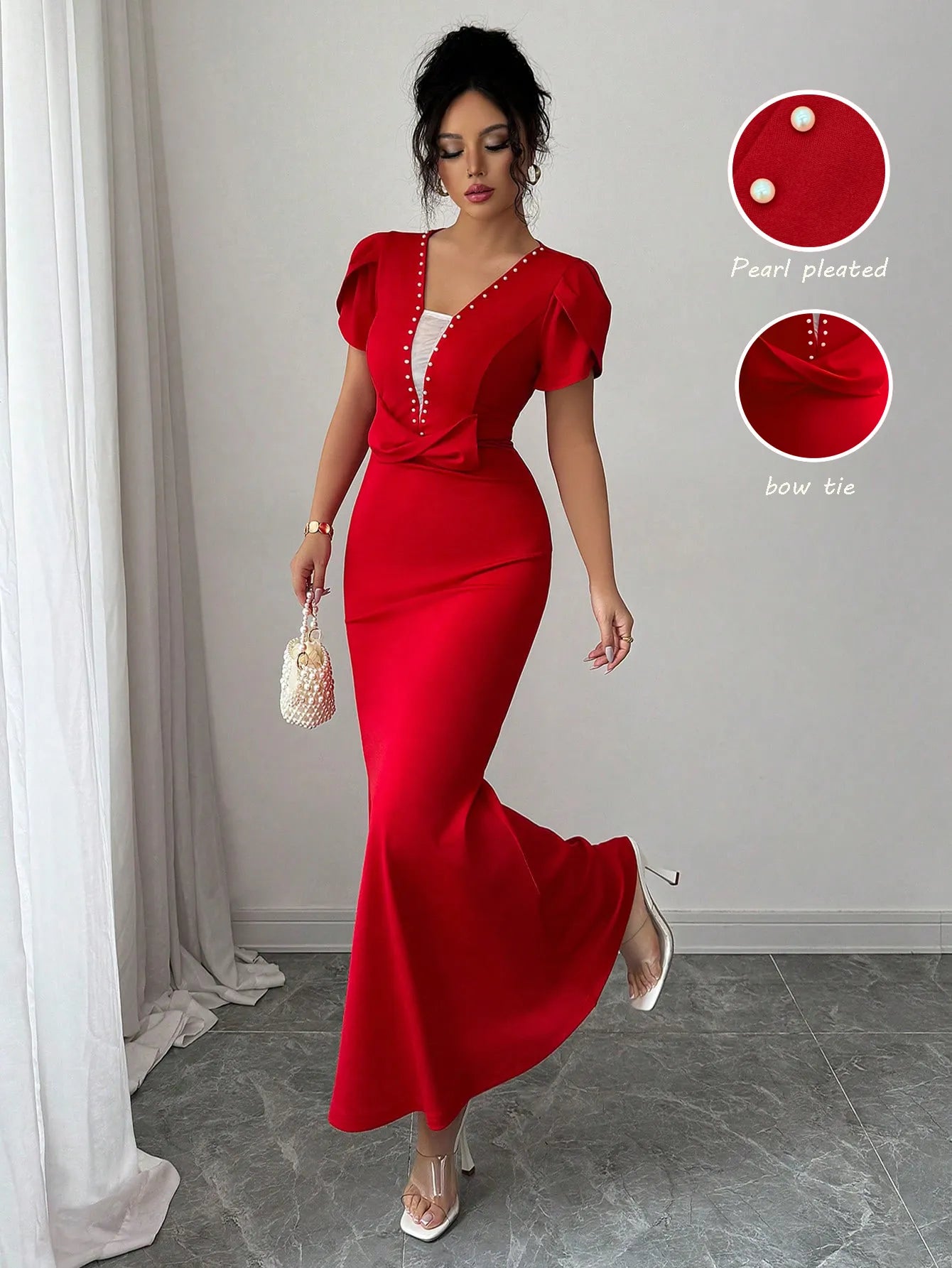 Woman wearing a red dress with pearl pleated details and bow tie, standing in a room with white curtains.