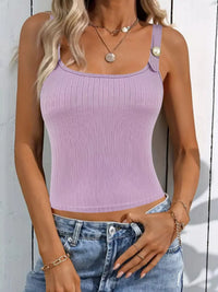 Woman wearing a purple ribbed tank top and blue jeans against a white wall.