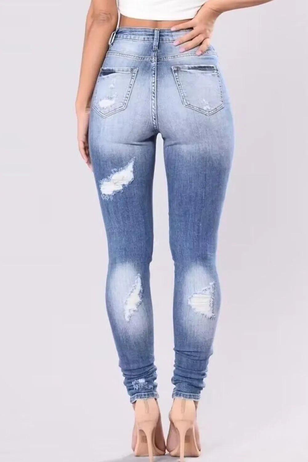 Light blue distressed jeans worn by a person on a gray background