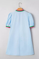 Light blue dress with green and pink trim on a hanger against a gray background