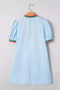 Light blue dress with green and pink trim on a hanger against a gray background