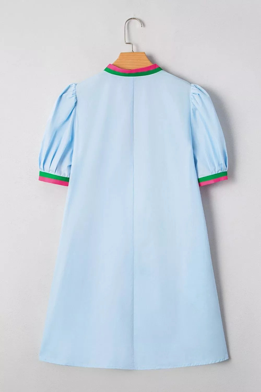 Light blue dress with green and pink trim on a hanger against a gray background