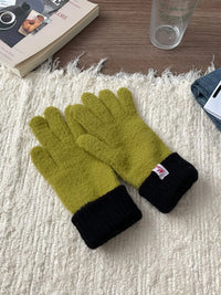 Pair of green gloves with black cuffs on a textured surface.