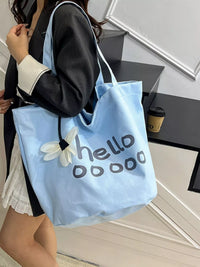 Person holding a light blue tote bag with 'hellooooo' text and a white flower design.