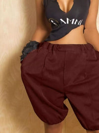 Person wearing a black crop top with white text and maroon shorts on a beige background
