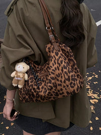 Person wearing a leopard print bag with a teddy bear charm, standing on a street.
