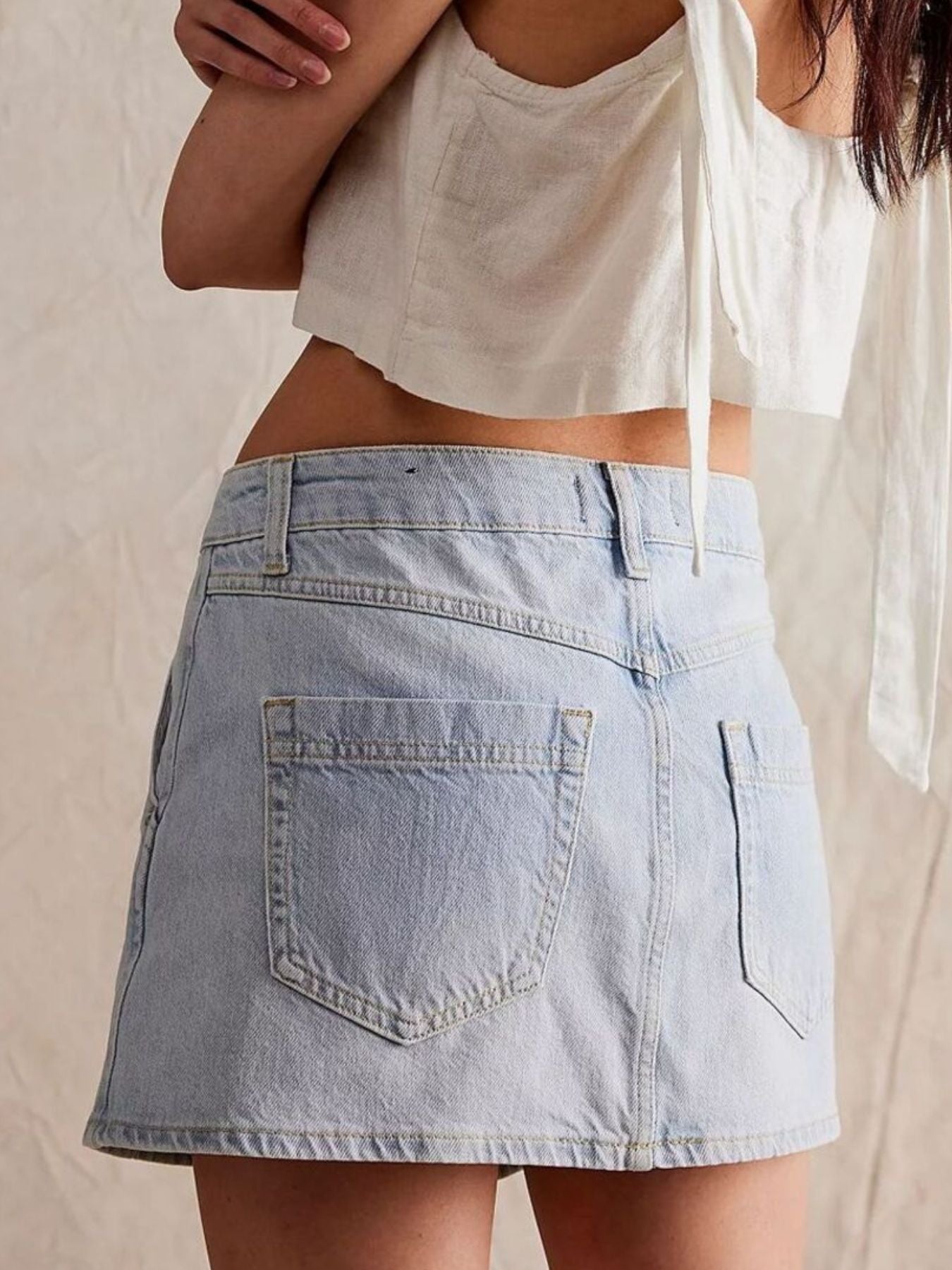 Person wearing a light blue denim skirt and white crop top against a neutral background