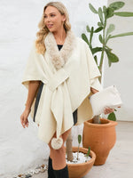 Woman wearing a cream-colored poncho with pom-poms in an indoor setting with plants.