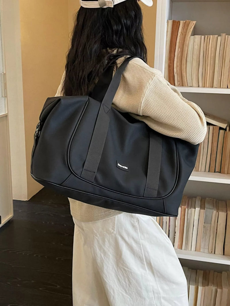 Person holding a black duffel bag in a room with bookshelves.
