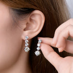Close-up of a person wearing diamond earrings with a hand adjusting them.