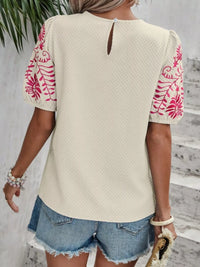 Person wearing a beige top with pink floral patterns and denim shorts indoors.