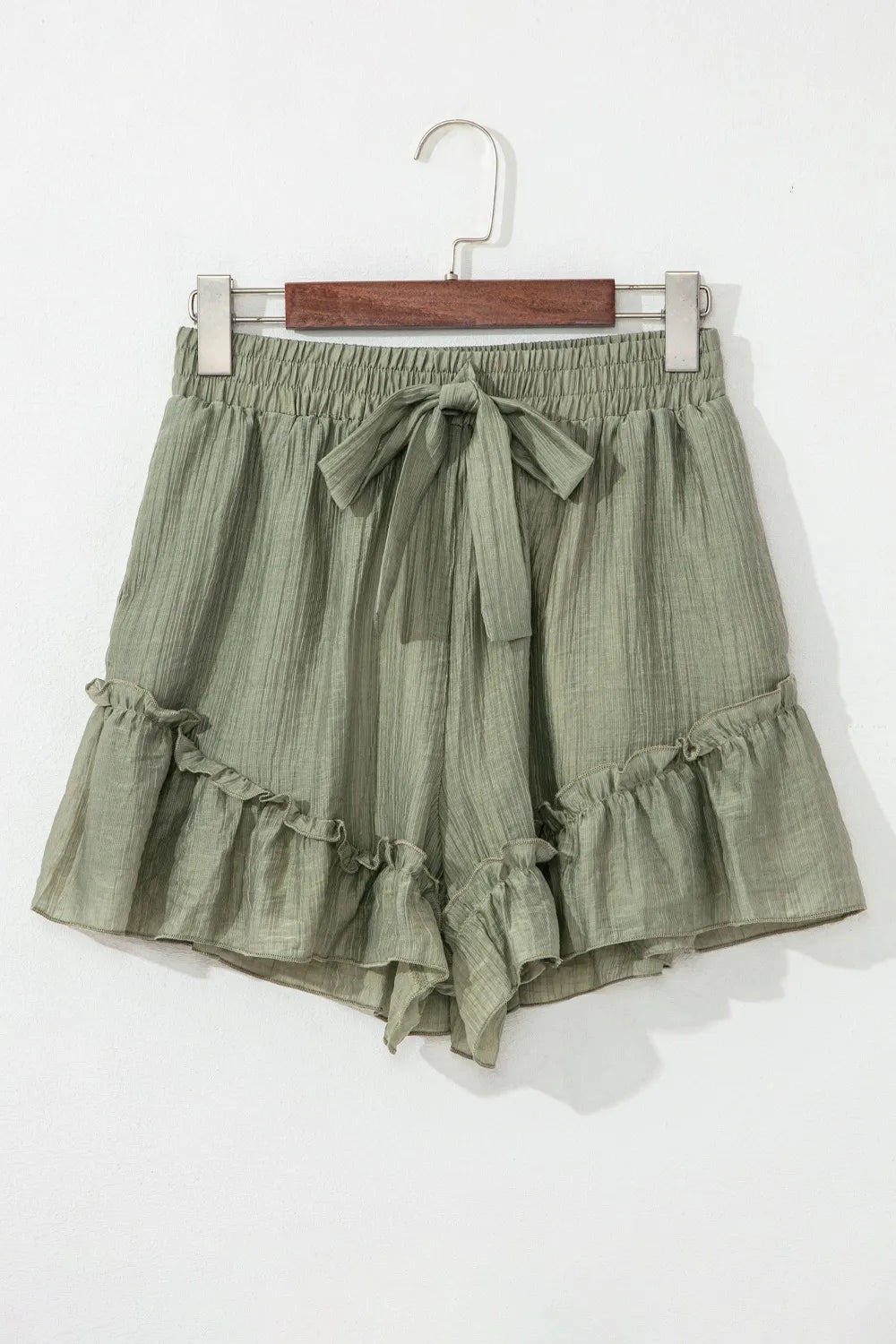 Green ruffled shorts on a hanger against a white background