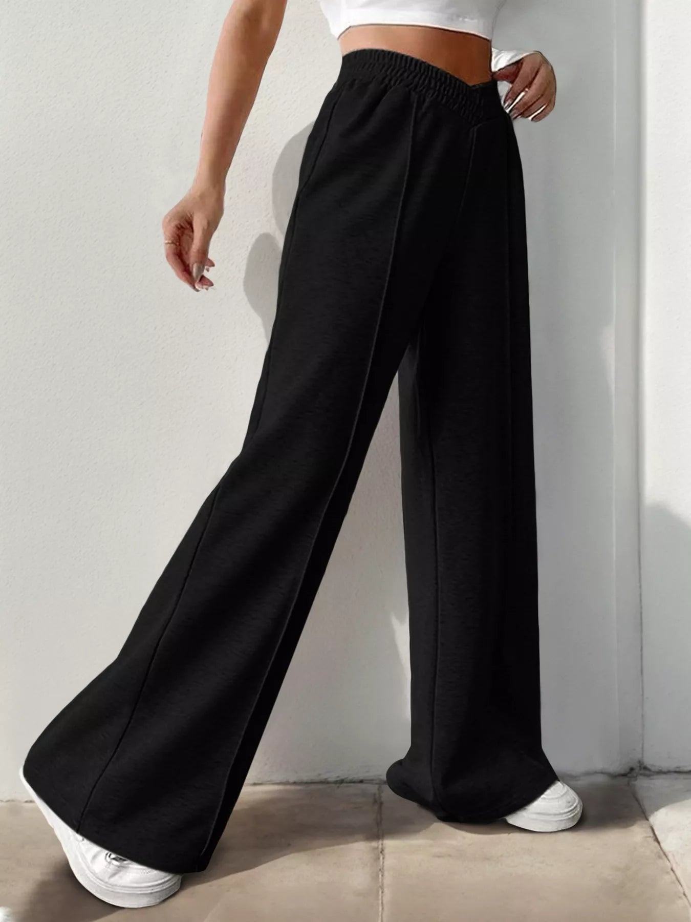 Person wearing black wide-leg pants and white sneakers against a plain background
