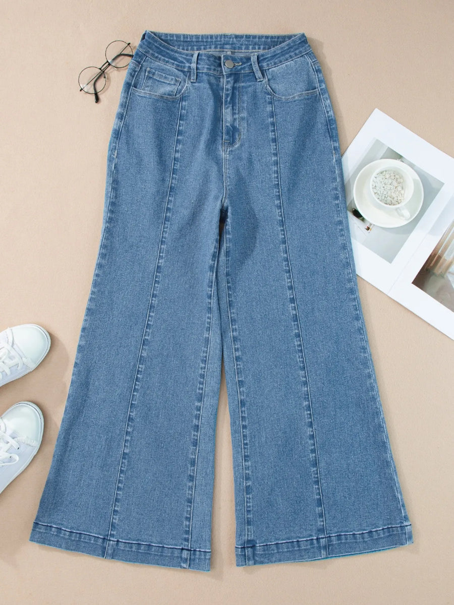 Blue jeans on a beige surface with white sneakers and a magazine.