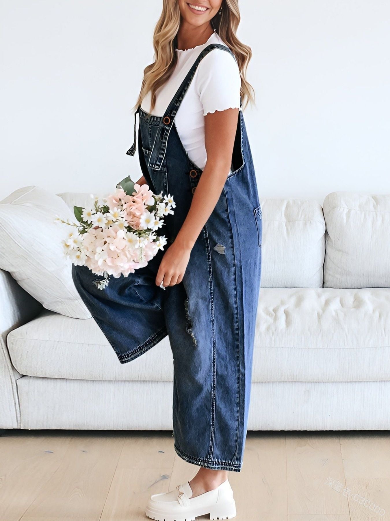 Person wearing denim overalls holding flowers in a living room setting