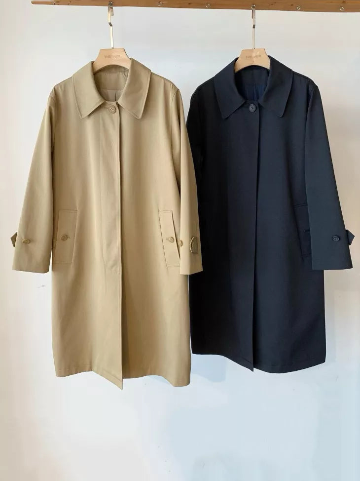 Two long trench coats hanging on wooden hangers against a plain white wall. The coat on the left is a light tan/khaki color, and the coat on the right is a dark navy blue.