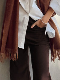 Person wearing a white shirt, brown pants, and a brown scarf against a neutral background