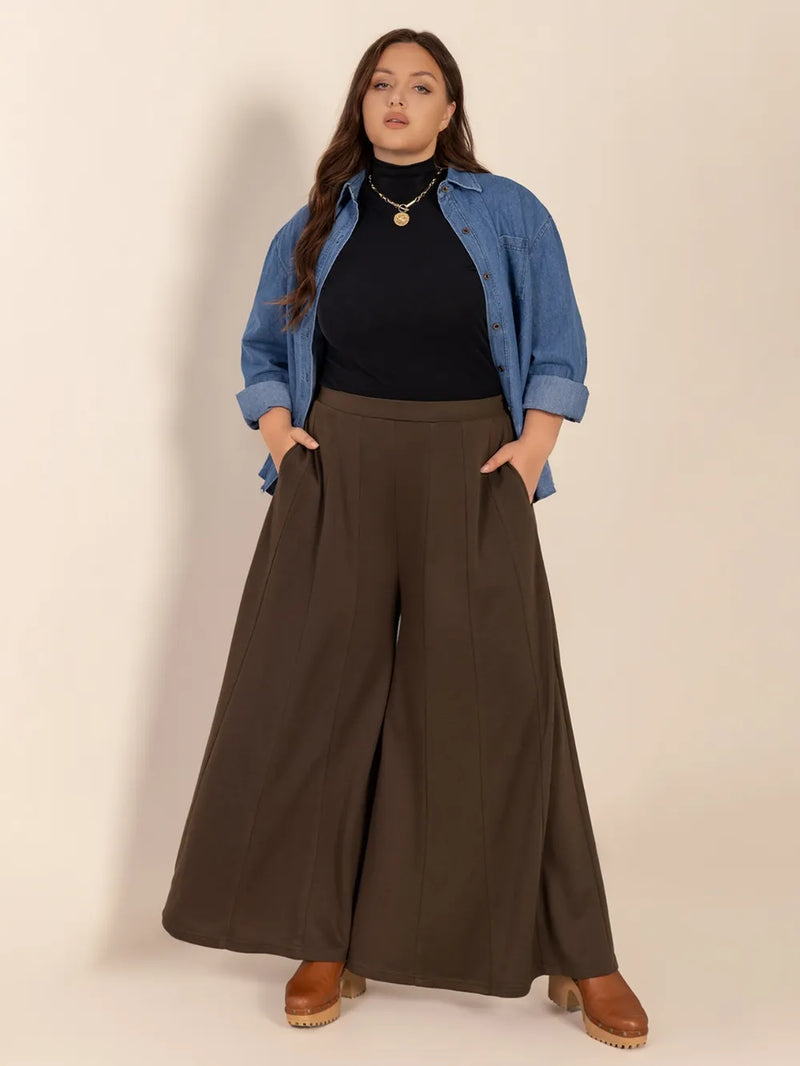 Woman wearing a blue denim jacket, black top, and brown wide-leg pants against a beige background