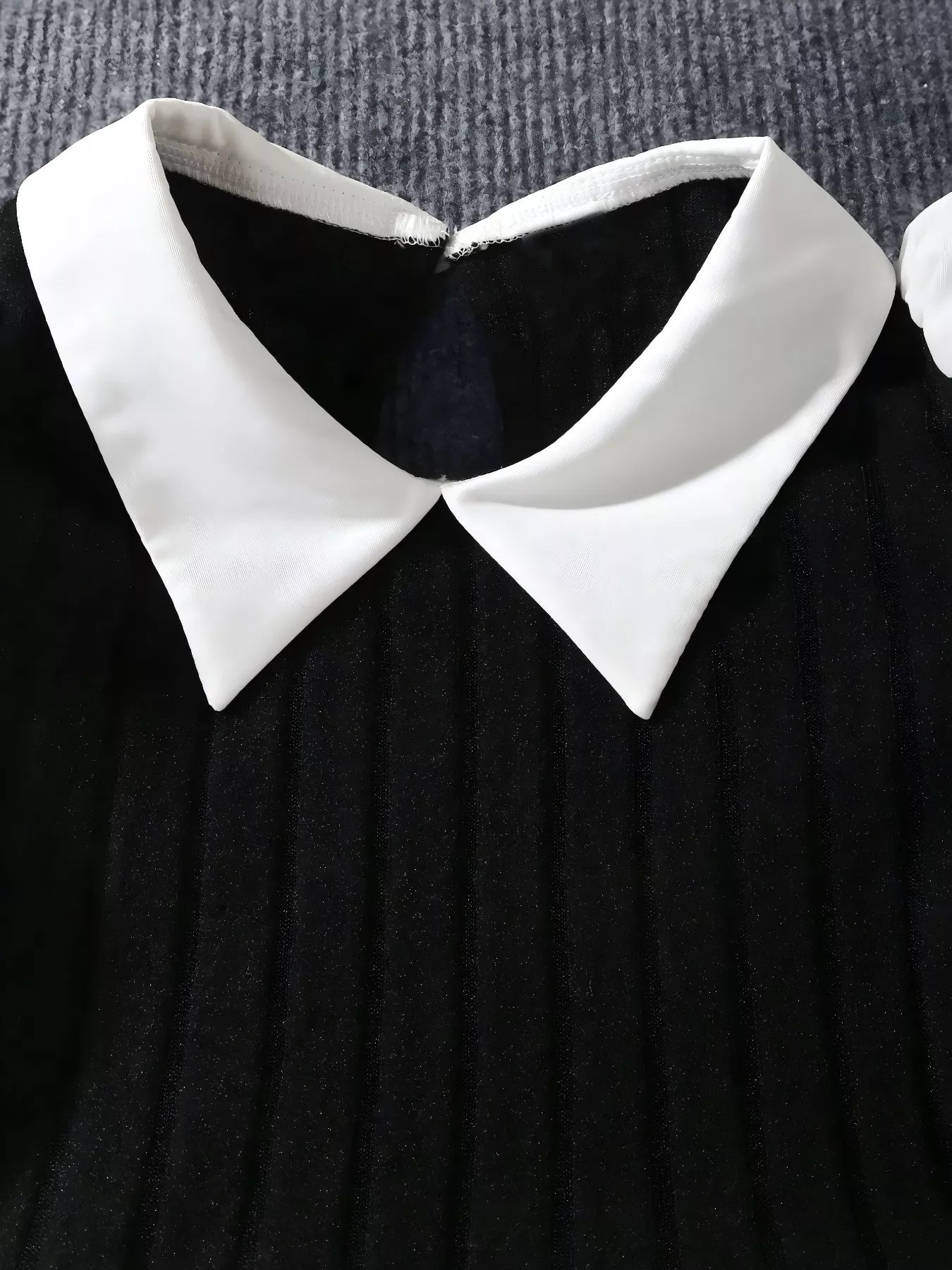 Black dress with a white collar on a textured gray background