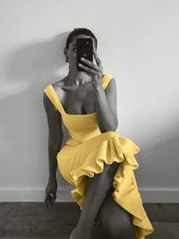 Person wearing a yellow dress sitting against a plain wall.