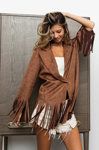 Woman wearing a brown suede jacket with fringe in front of a wooden cabinet.