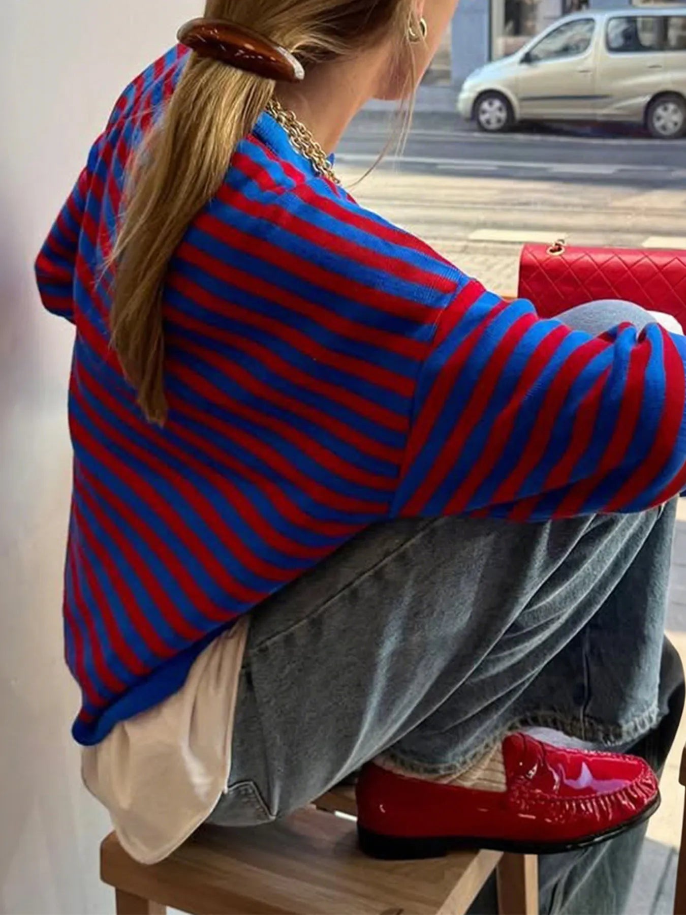 Person wearing a red and blue striped sweater sitting on a chair with a blurred background