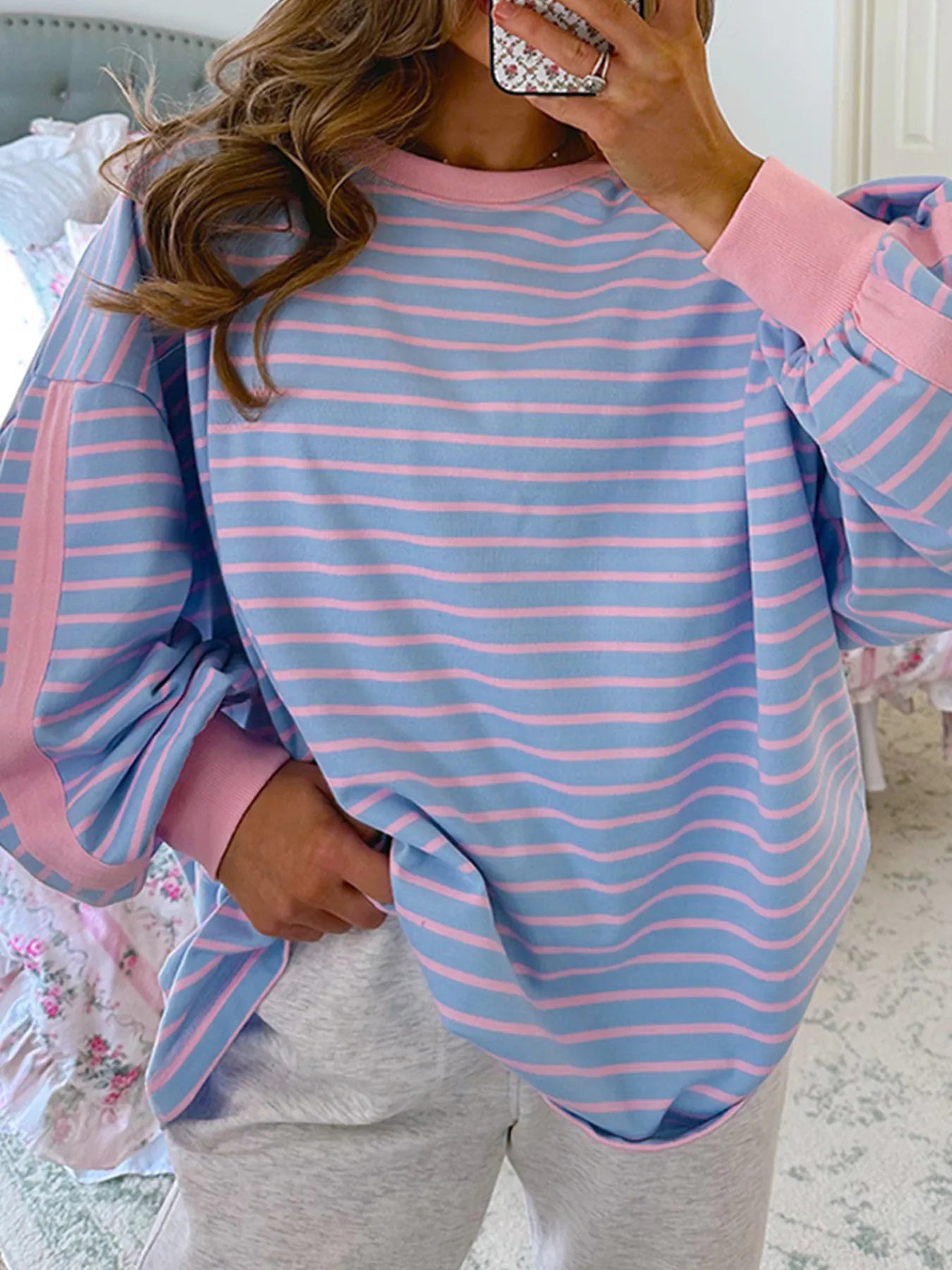 Person wearing a blue and pink striped long-sleeve top with gray pants indoors.