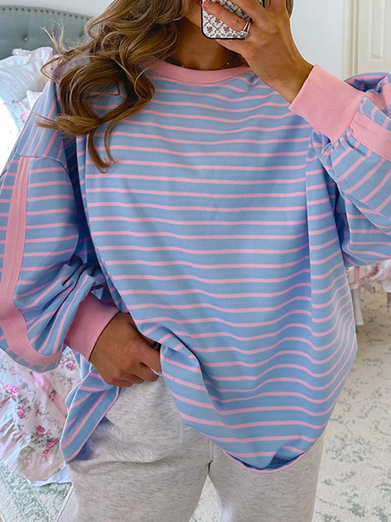 Person wearing a blue and pink striped long-sleeve top with gray pants indoors.