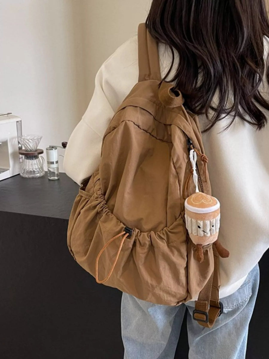 Person holding a brown backpack with a small plush toy attached, wearing a white shirt and light blue jeans.
