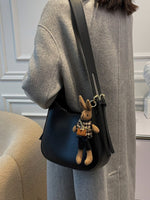Person wearing a gray coat with a blue bag featuring a teddy bear charm.