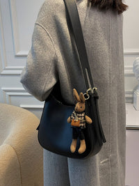 Person wearing a gray coat with a blue bag featuring a teddy bear charm.