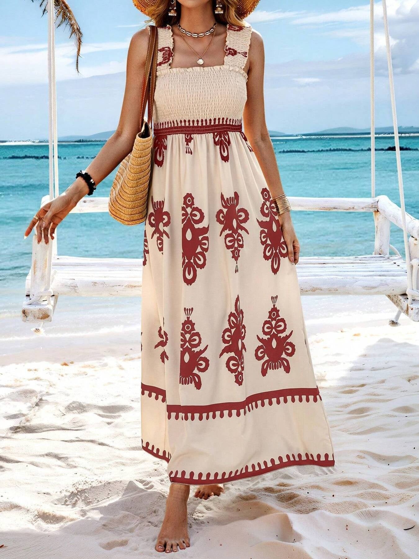 Woman in a long, patterned dress standing on a sandy beach with ocean view.