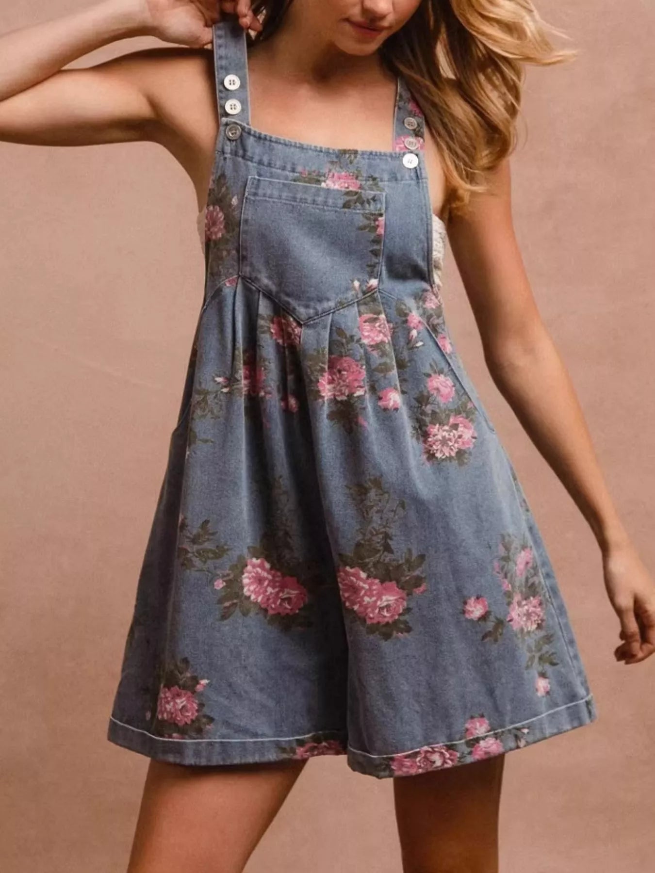 Denim pinafore dress with floral pattern worn by a person on a beige background
