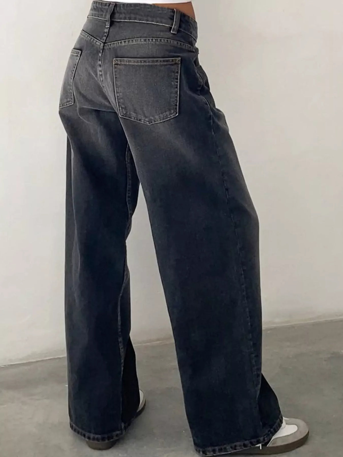 A person wearing dark gray wide-leg jeans, shown from the back, standing against a plain light gray wall.