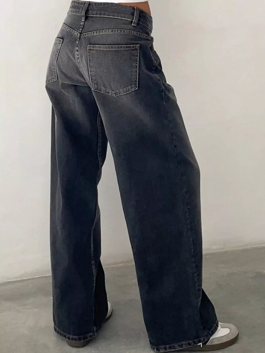 A person wearing dark gray wide-leg jeans, shown from the back, standing against a plain light gray wall.