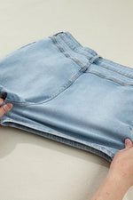 Light blue denim shorts being held on a plain background