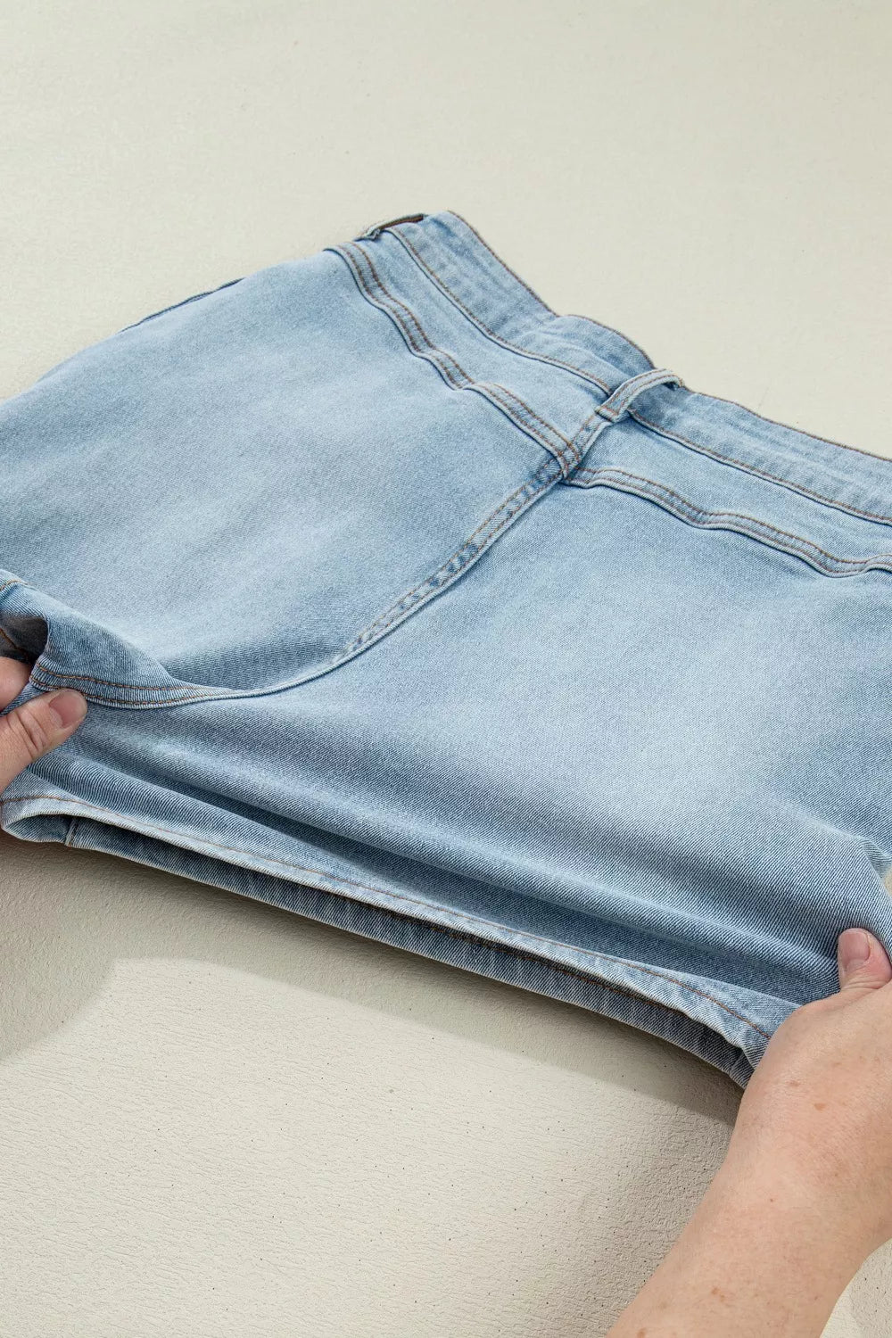 Light blue denim shorts being held on a plain background