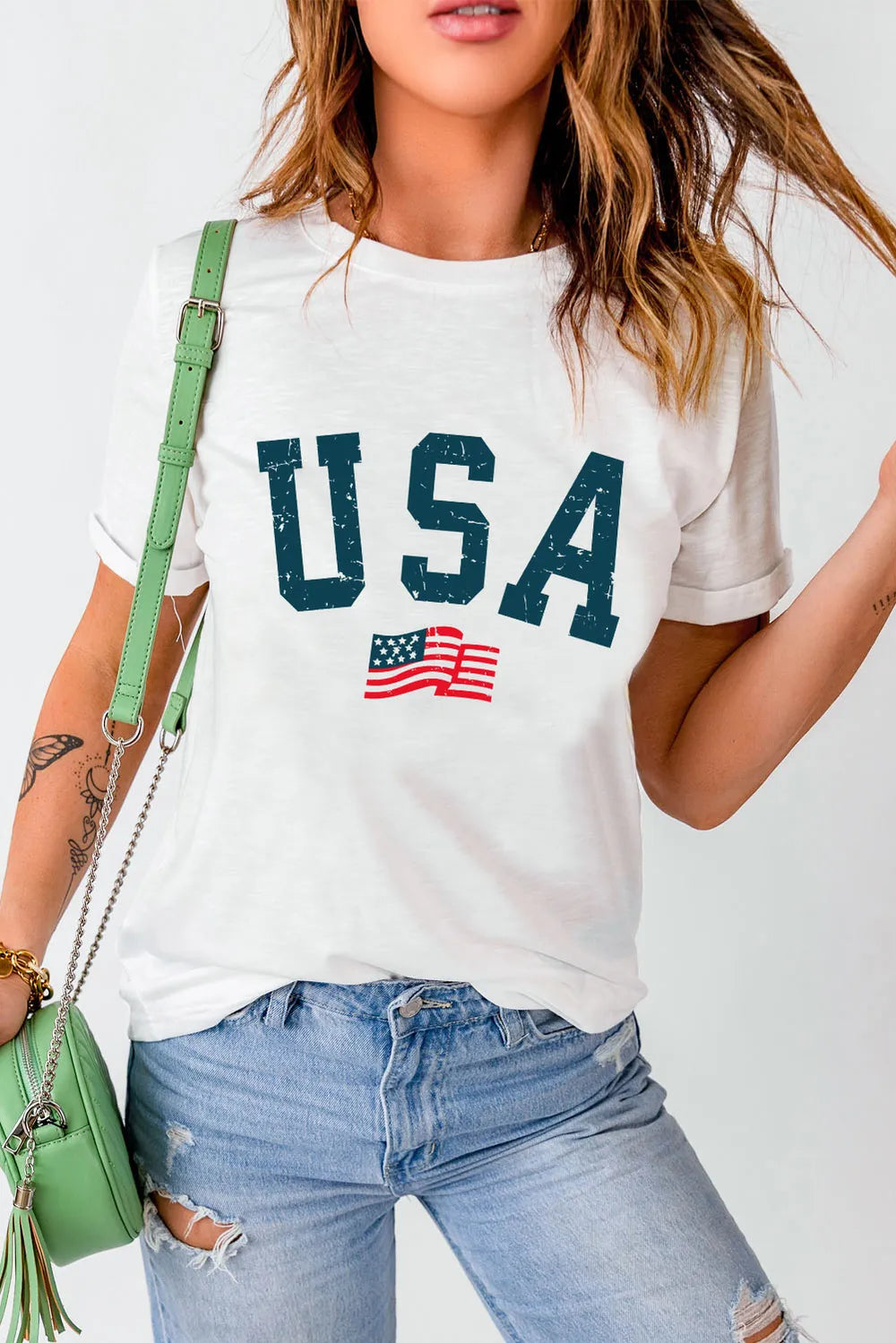 Person wearing a white t-shirt with 'USA' and an American flag graphic, holding a green handbag.