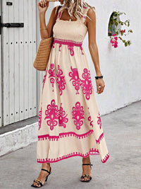 Woman wearing a beige dress with pink patterns, standing against a white wall.