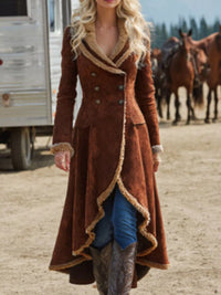 Woman wearing a long brown coat with fur trim standing in front of horses and a trailer.