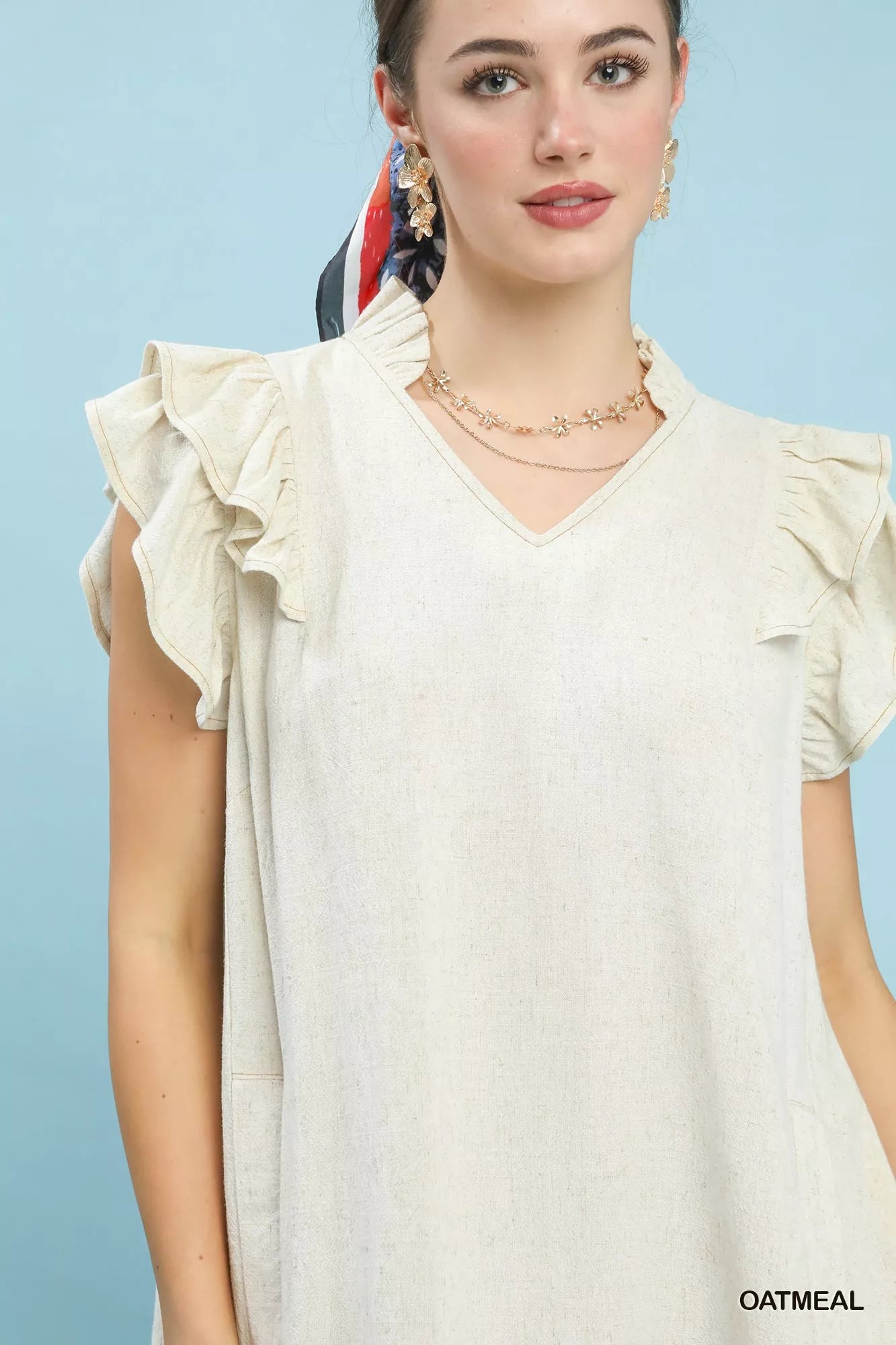 Woman wearing a light-colored blouse with ruffled sleeves against a light blue background