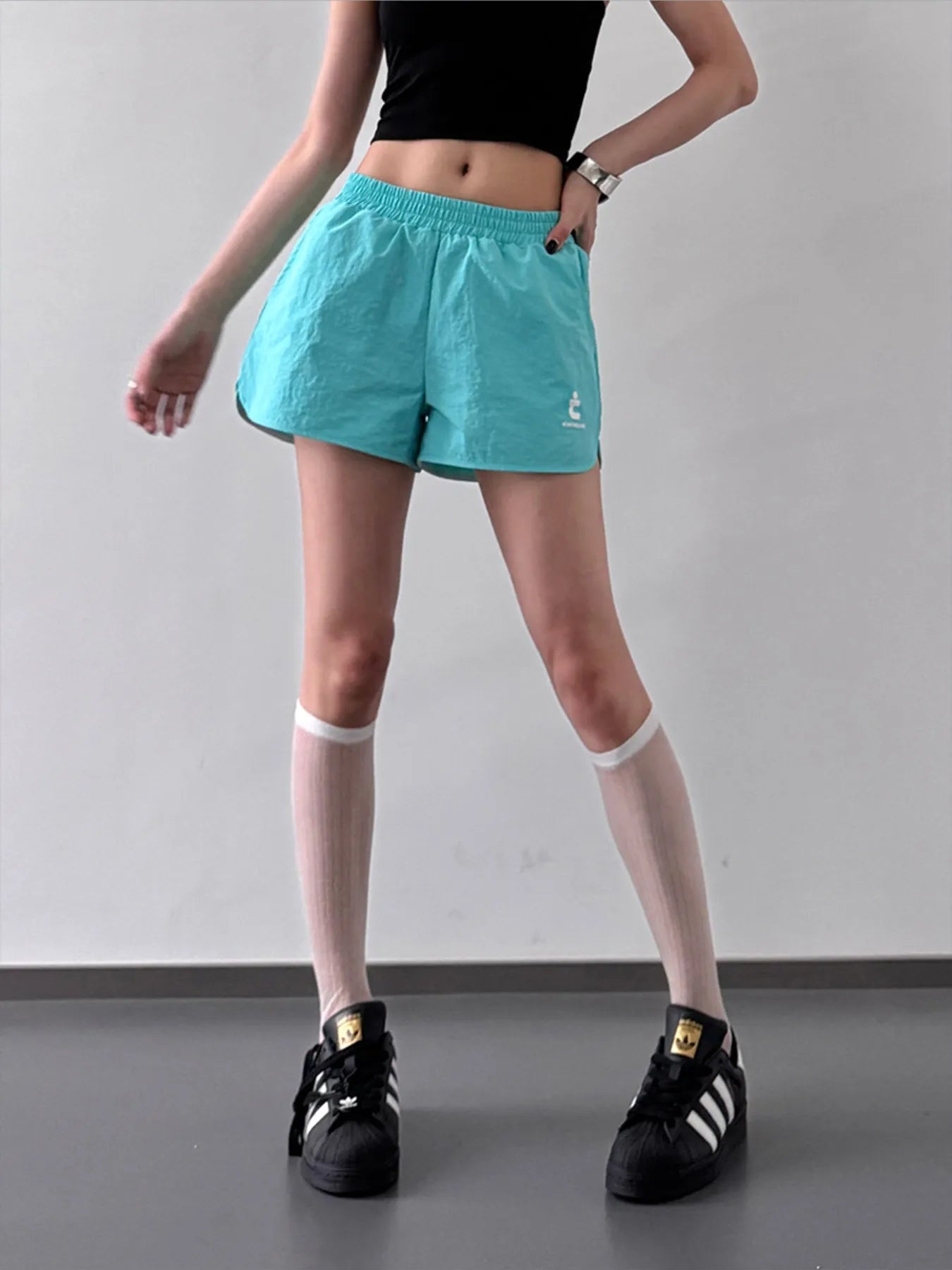Person wearing teal shorts and black Adidas shoes on a plain background