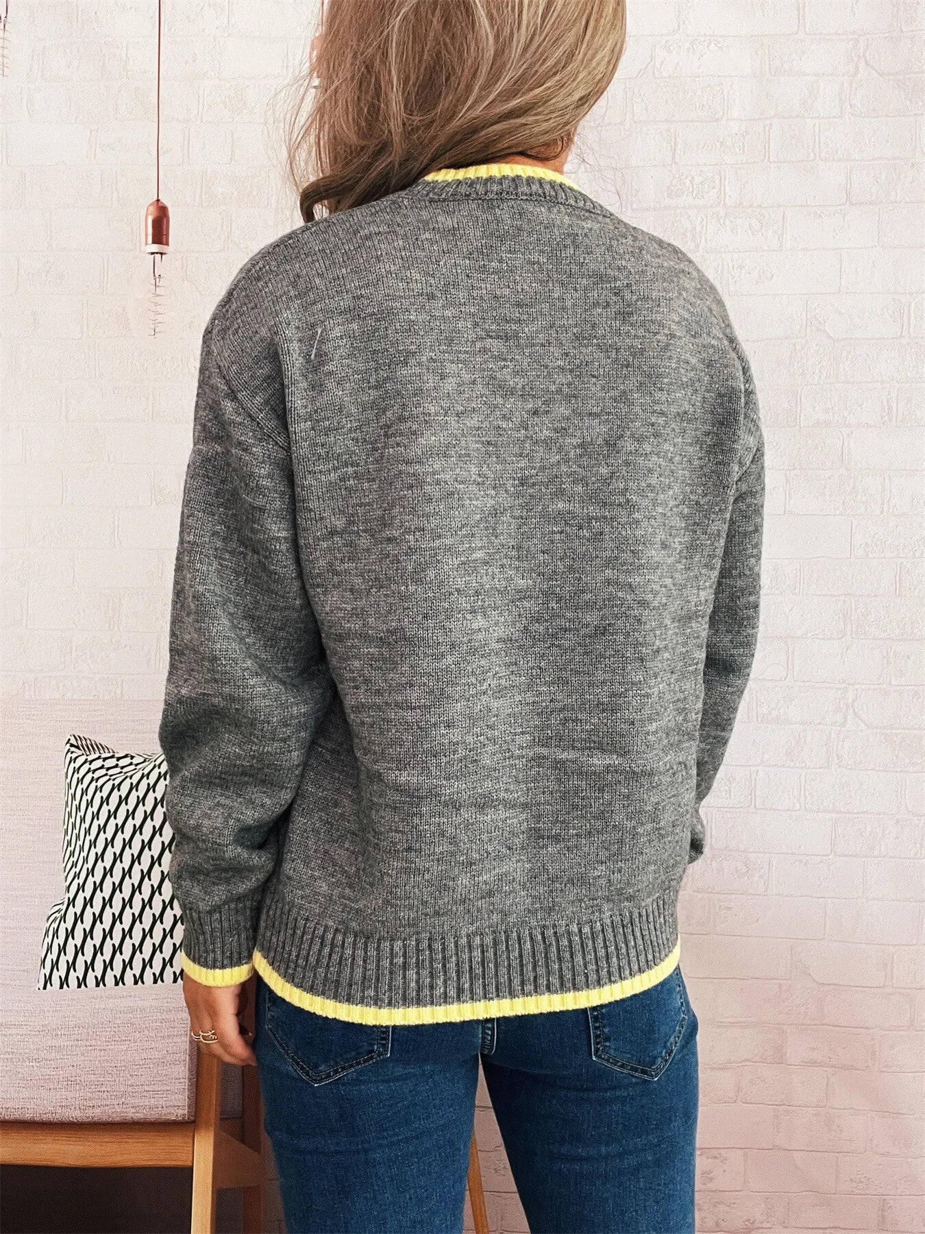 Person wearing a gray sweater with yellow trim, standing against a light-colored wall.