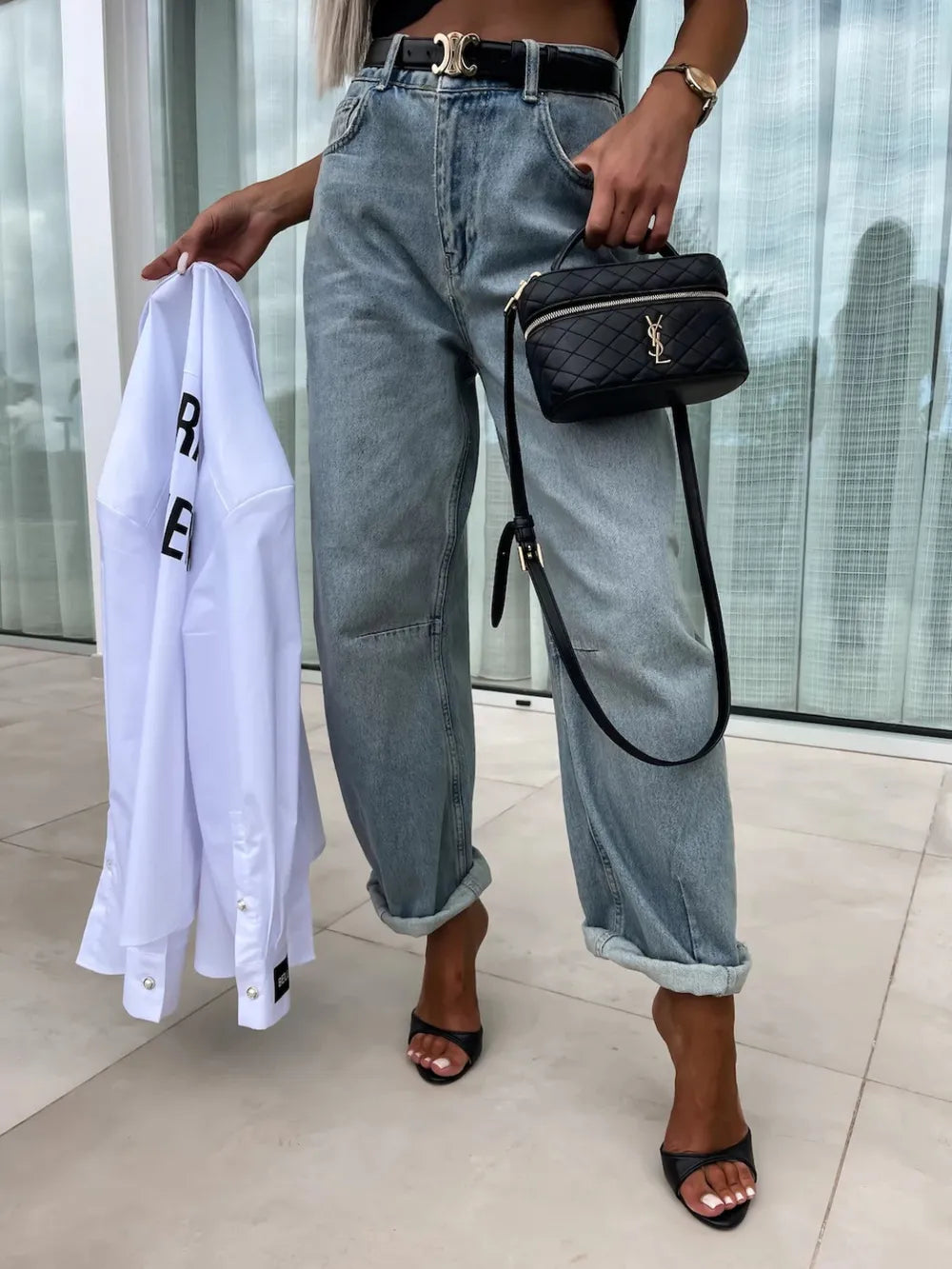 Person holding a white shirt and black handbag with a blurred background