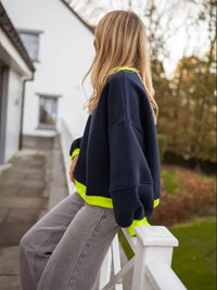 Person wearing a navy sweatshirt with bright yellow accents, standing on a white railing outdoors.