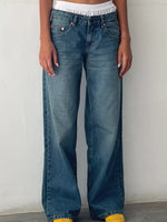 A person wearing medium-wash blue wide-leg jeans, shown from the waist down against a plain off-white wall.