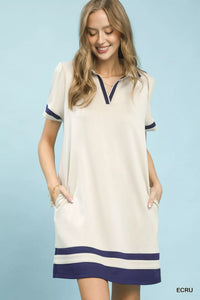Woman wearing a cream dress with navy accents on a light blue background